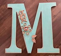 Front view of turquoise wood letter “M” with metal floral embellishments
