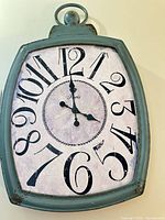 Front view of teal wall clock showing face, numerals and distressed frame
