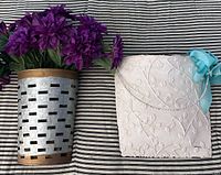 Both wall pockets side by side, metal pocket filled with purple flowers, white embossed pocket with rope and ribbon