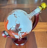 Full view of globe decanter on wooden stand with brass stopper