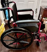 Side view showing red frame, black composite 24" wheels, padded armrests, footrests