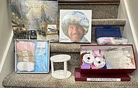 All items arranged on stairs: paint-by-number kit, Bob Ross game, baby knitting kit, rotating marker holder, box of paper shapes, box of lace and ribbon