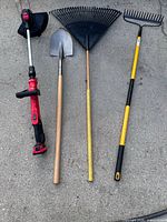 Full view of all four tools laid out: Craftsman string trimmer, steel shovel, plastic fan rake, metal bow rake