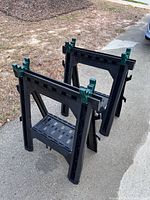 Two black plastic folding sawhorses standing upright on driveway