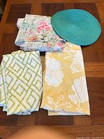 Folded shower curtains showing three different patterns and one teal placemat on wooden table