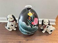 Front view of two Staffordshire dog figurines flanking black floral vase