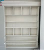 Front view of white wooden wall-mounted craft shelf with cubbies and ribbon rods