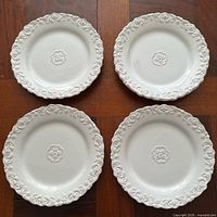 Four white salad plates with embossed rim and center medallion arranged in grid