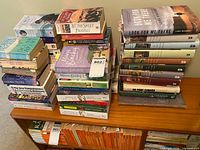 Wide view of three stacks of assorted hardcover & paperback novels on wooden shelf