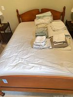 Full view of maple bed frame with mattress and folded linens
