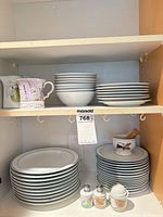 Stacks of plates, bowls, mugs, shakers on cabinet shelves