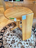 Round solid wood dining table with leaf leaning against it