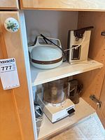 Cuisinart food processor, Sunbeam can opener and unidentified dome-top appliance in cupboard