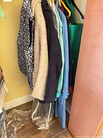 Five coats/jackets hanging: patterned quilted, beige wool, navy wool, aqua raincoat, blue trench plus plastic cover bottom visible