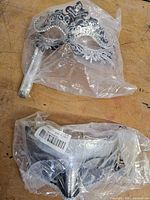 Both silver filigree masks in individual plastic sleeves, one with handle visible