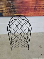 Full view of black metal arched floor wine rack standing on concrete