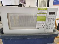 Front view of white Hamilton Beach countertop microwave showing keypad, display, door and quick start guide tag
