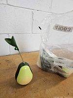 One assembled avocado cat toy with stem and bell beside bag containing two additional identical toys