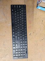 Top view of black slim wireless keyboard on workbench, partial retail box in corner