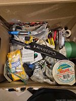 Top view of box showing mixed tools, hardware, tapes, Cuisinart sheath, margarine lid
