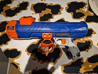 Full view of blue and orange Nerf Dog ball launcher lying on patterned surface