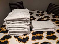 Stack of five folded bath towels beside three folded hand towels on table