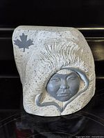 Front view of speckled stone hooded face sculpture with maple leaf