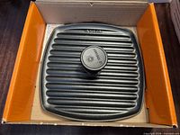 Panini press in open box showing ridged surface and knob