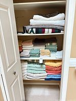 Closet shelves filled with stacked bath towels, hand towels, washcloths and mats in various colors
