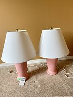 Pair of pink ceramic lamps with shades and cords visible