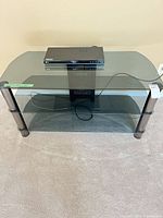 Front view of stand showing three glass tiers and Blu-ray player on top