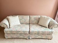 Front view of pastel floral 3-seat sofa with two cream throw pillows
