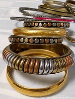 Stacked view of ribbed tri-colour, studded, smooth and hammered bangles