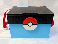 Closed carry case showing Poké Ball clasp, black lid, light blue base, red carrying strap