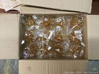 Open cardboard box showing multiple gold starburst Christmas ornaments individually bagged in plastic and neatly arranged inside the box.
