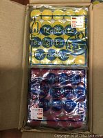 Close-up photo of two packages of tea light candles, one yellow and one dark red, in sealed plastic packaging in a cardboard box.