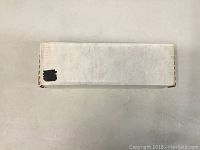 Closed white cardboard box containing the cards, viewed from the side.