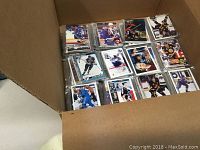 Open box showing multiple hockey cards stacked in protective sleeves, featuring players in various NHL team uniforms.