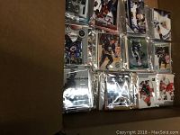 Photo showing a partial view of numerous sealed NHL hockey card packs inside a box, displaying various player images on the front of packs.