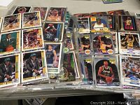 Photo showing multiple binder pages with basketball trading cards, various players shown, cards in plastic sleeves across pages.
