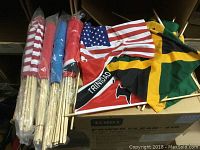 Close-up photo showing several rolled and folded flags with wooden poles visible, including the USA flag and Trinidad flag.