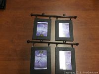 Two black metal photo frame hangers each with two black rectangular picture frames attached, displayed on a wood surface. Frames hold placeholder photos.