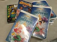 Photo of six VHS Disney movies including four copies of The Little Mermaid with original art covers and two sealed VHS tapes for So Dear to My Heart and The Jungle Book.