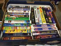 VHS tapes stacked in a box, showing titles such as Scooby-Doo, Casper, Alaska, Aladdin, Dumbo, Elmo, and more.