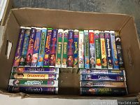 Box filled with assorted used VHS movies predominantly Disney titles including The Lion King, Aladdin, Bambi, Pocahontas, Sleeping Beauty.