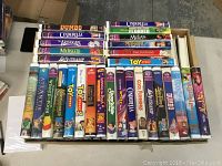 Box top view showing a variety of mostly Disney VHS movies including Dumbo, Cinderella, The Aristocats, Mulan, Lady and the Tramp, 101 Dalmatians, Toy Story series, Atlantis, Winnie the Pooh; cases show signs of wear.