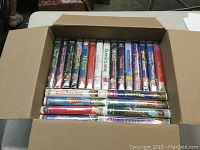 Box of assorted used VHS movies showing titles including Beauty and the Beast, The Jungle Book, Aladdin, The Santa Clause, Peter Pan, Goofy Movie, Down Under, and The Lion King.