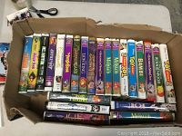 Top view of assorted VHS tapes in a cardboard box with titles including Jungle Book, Lion King, Toy Story, Bambi, Winnie the Pooh and others