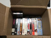Box with assorted used VHS movies showing titles like Dial M for Murder, Striking Distance, Speed, Titanic.