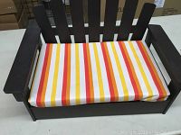 Small wooden pet bed with a dark finish, featuring a slatted backrest and a thick cushion covered in striped fabric.